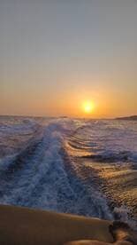 A stunning sunset over the ocean, with waves trailing behind a boat, creating a picturesque scene perfect for evening cruises.