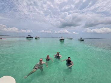 A group of friends enjoys a refreshing swim in crystal-clear turquoise waters, surrounded by boats — a perfect day for snorkeling and relaxation.