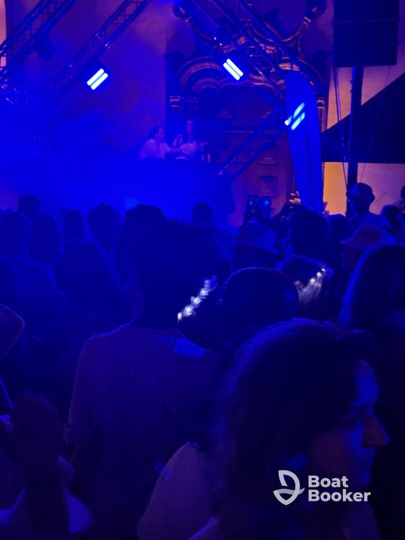 A vibrant scene from a crowded event with a DJ performance, illuminated by blue lights, creating an energetic atmosphere.
