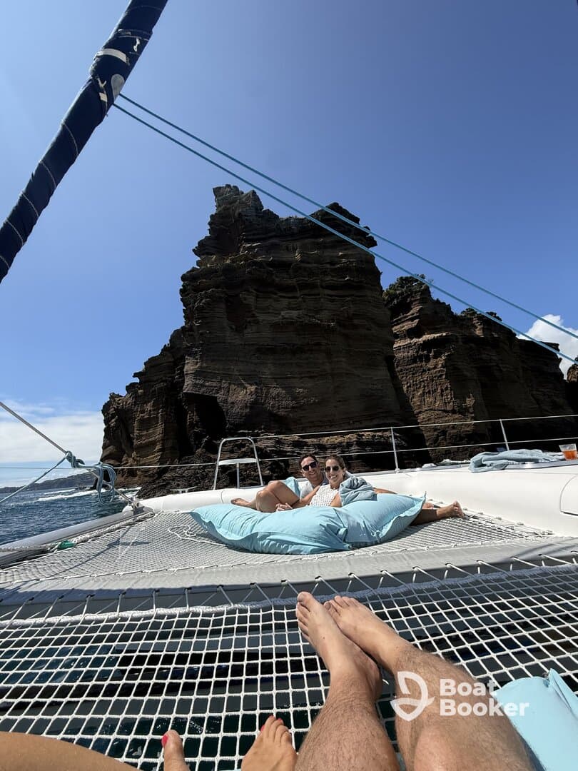 A couple relaxes on the netting of a catamaran, enjoying stunning rock formations and clear waters — a perfect getaway for scenic views and relaxation.