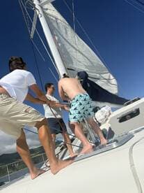 A group of friends actively sailing on a catamaran, working together to adjust the sails under a clear blue sky — a perfect day for adventure on the water.