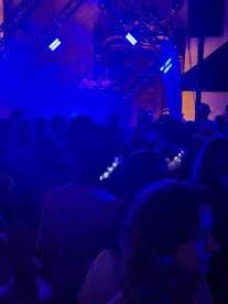 A vibrant scene from a crowded event with a DJ performance, illuminated by blue lights, creating an energetic atmosphere.