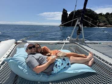 A couple relaxes on a catamaran's netting, enjoying the sun and ocean views — perfect for a romantic getaway or a day of leisure on the water.