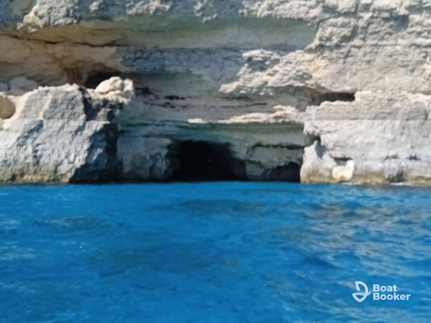 An unclear view of a rocky cliffside with a cave entrance, surrounded by vibrant blue waters. The image lacks clarity and detail.