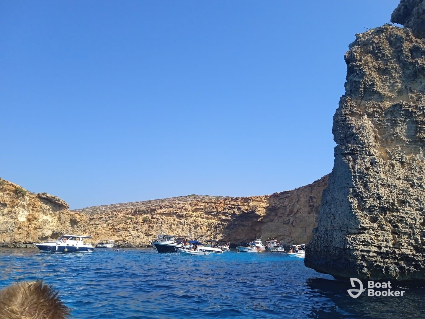 A picturesque view of multiple boats anchored near a stunning coastline, showcasing the vibrant blue waters and rocky cliffs — perfect for a day of exploration and adventure.
