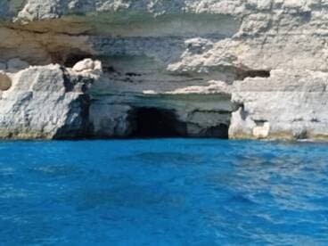 An unclear view of a rocky cliffside with a cave entrance, surrounded by vibrant blue waters. The image lacks clarity and detail.