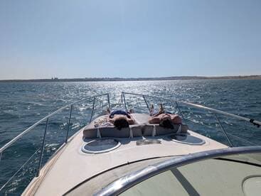 Two individuals relax on the bow of a boat, enjoying the sun and the serene waters — a perfect moment for unwinding on a summer day.