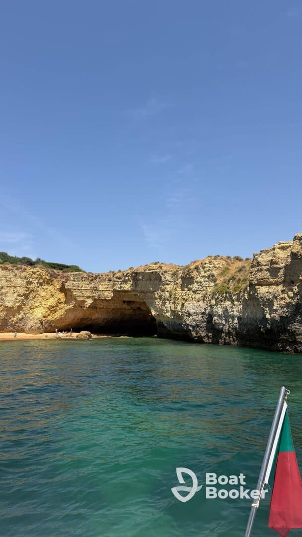 A stunning view of a coastal cave with a sandy beach, where visitors can be seen enjoying the picturesque scenery — a perfect spot for exploration and relaxation.