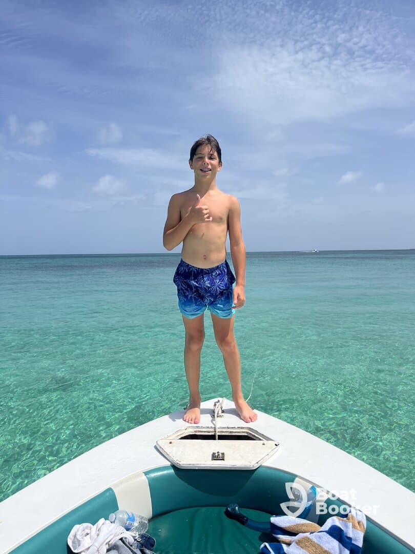 A young boy stands on the bow of a boat, giving a thumbs up against a backdrop of clear turquoise waters — a perfect moment of joy on a boating adventure.