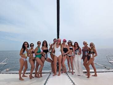 A lively group of women enjoying a fun day on a yacht, celebrating with drinks and smiles against a beautiful ocean backdrop.