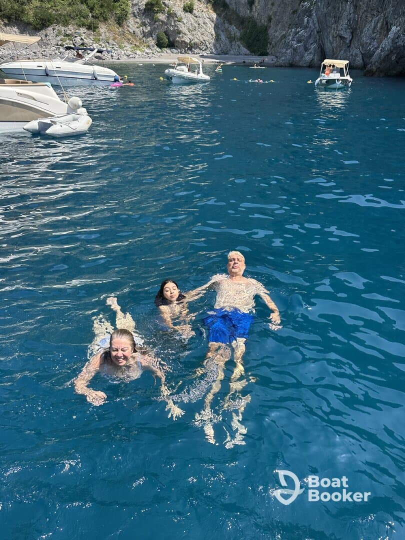 A joyful group enjoys swimming in crystal-clear waters, surrounded by boats and a beautiful beach backdrop — perfect for summer adventures.