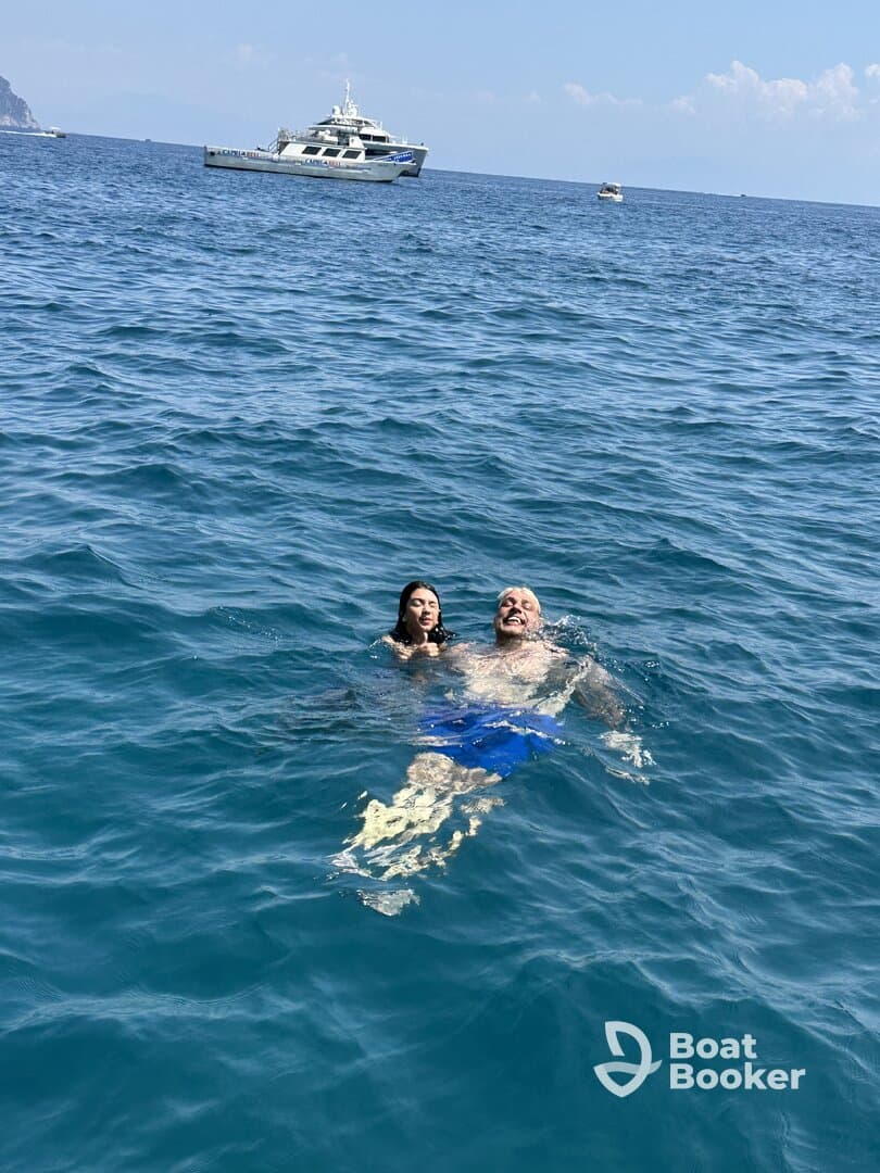 A couple enjoys a refreshing swim in the ocean with a boat in the background, capturing the essence of a perfect day on the water.