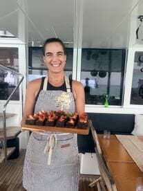 A smiling chef presents a beautifully arranged platter of brownies topped with strawberries aboard a luxurious yacht, showcasing the culinary delights available for guests.