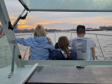 A group enjoys a scenic sunset view from the back of a boat, with a vibrant city skyline in the background — perfect for evening cruises and memorable outings.