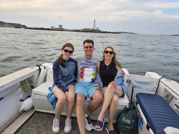 A family enjoys a relaxing moment on a boat with a scenic lighthouse in the background, perfect for memorable outings on the water.