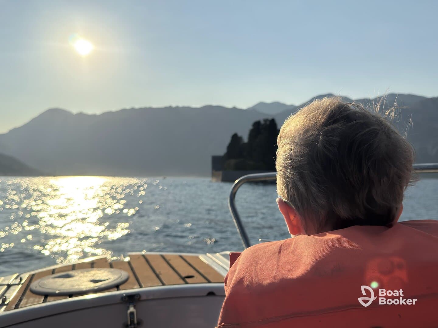 A child in a life jacket gazes at the sunset from the boat, creating a serene moment amidst stunning mountain scenery — perfect for family adventures on the water.