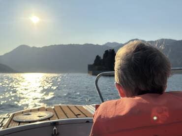A child in a life jacket gazes at the sunset from the boat, creating a serene moment amidst stunning mountain scenery — perfect for family adventures on the water.