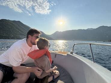 A father and son enjoy a serene moment on a boat, gazing at the sunset over the mountains — a perfect family outing on the water.