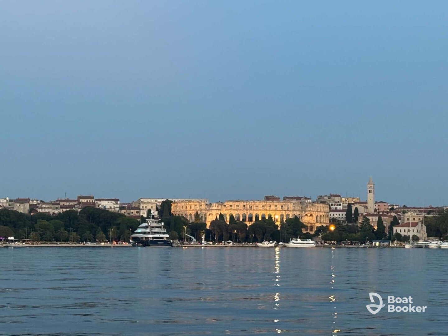 A picturesque view of a harbor at dusk, featuring a luxurious yacht and the illuminated architecture of the city in the background, perfect for showcasing scenic boating destinations.