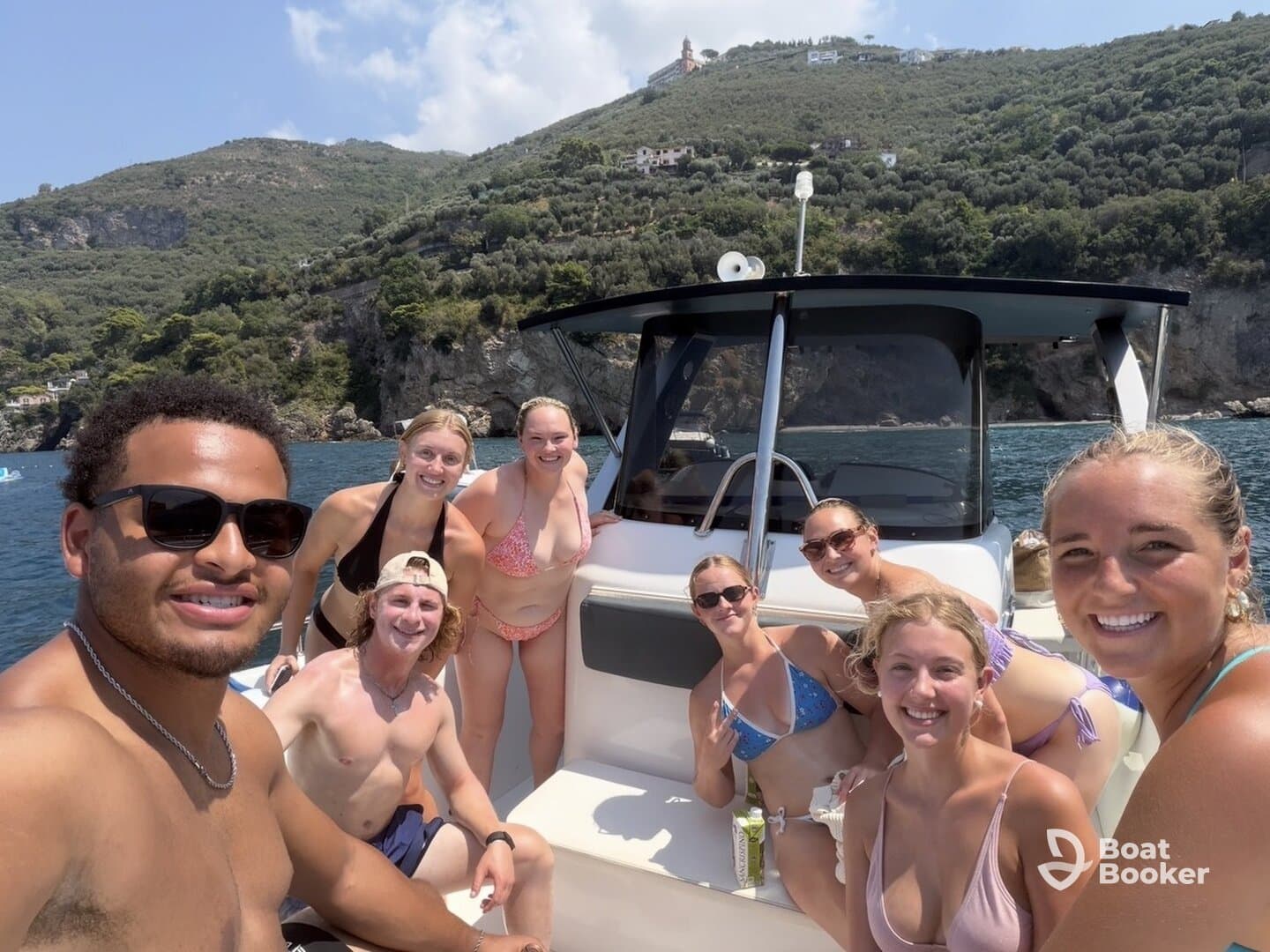 A lively group of friends enjoys a fun day on the boat, capturing memories against a stunning coastal backdrop — perfect for summer celebrations and adventures on the water.
