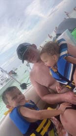 A father enjoys a fun day on the water with his two young children, all wearing life jackets, capturing a joyful family moment aboard a boat.