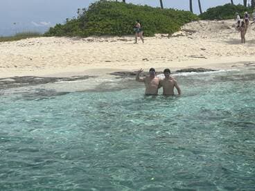 Two friends enjoy a refreshing swim in crystal-clear waters near a sandy beach, capturing the essence of a fun day in the sun.