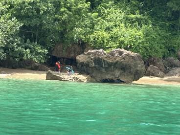 Two individuals explore a rocky beach area surrounded by lush greenery and clear turquoise waters, perfect for a day of adventure and relaxation.