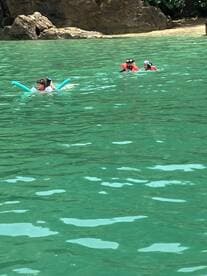 A family enjoys a fun day swimming in crystal-clear waters, with kids using pool noodles and snorkeling gear — a perfect beach adventure.