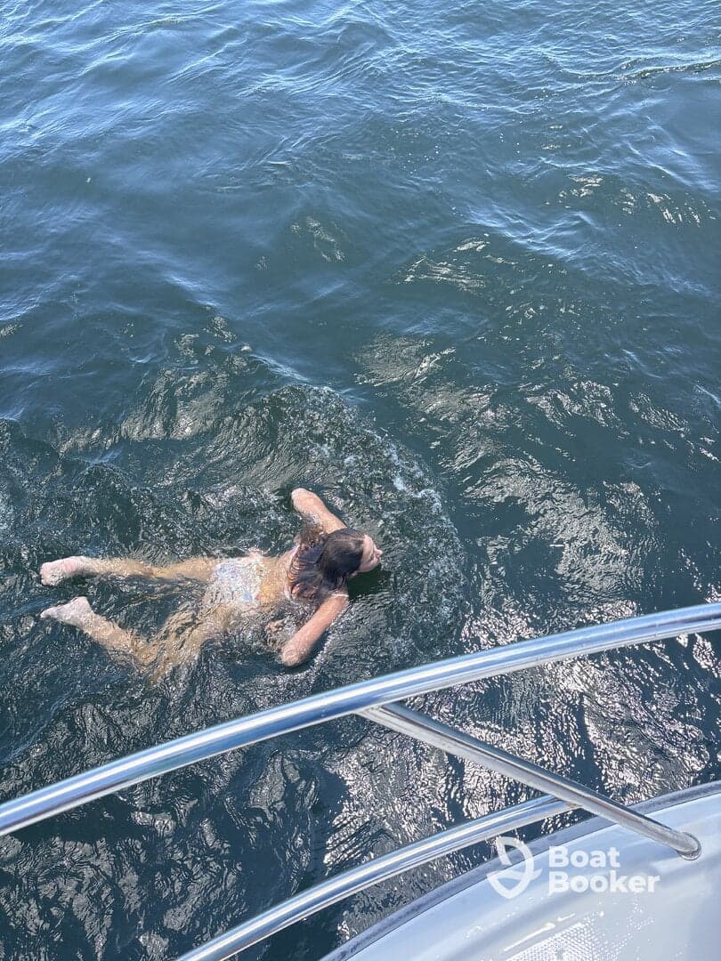 A person enjoys a refreshing swim in the open water, with a boat visible in the foreground — a perfect moment for summer fun on the water.