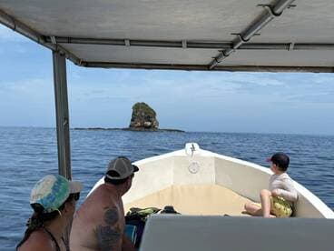 A family enjoys a scenic boat ride, gazing at a rocky island in the distance — a perfect moment for adventure seekers exploring the ocean.