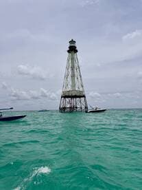 A stunning view of a lighthouse standing tall amidst turquoise waters, surrounded by boats — a picturesque landmark perfect for sightseeing and exploration.