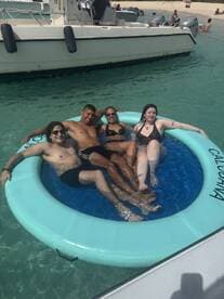A group of friends enjoys a sunny day floating in a mat on clear waters, perfect for beach fun and relaxation.