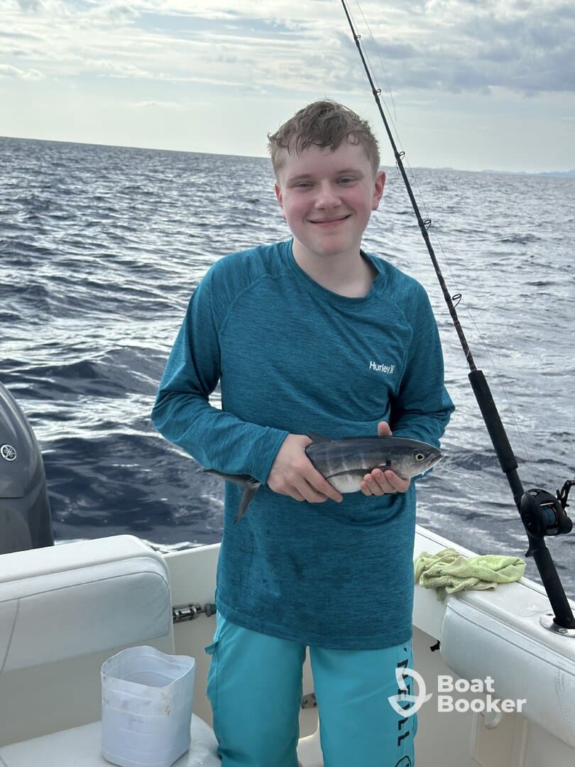 A young boy proudly holds up his catch while fishing on a boat in the open ocean, showcasing the excitement of a successful fishing trip.