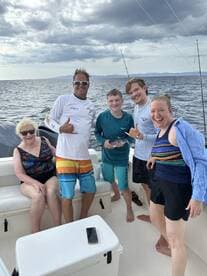 A joyful group poses for a photo on a fishing trip, showcasing their catch and enjoying a memorable day on the ocean.