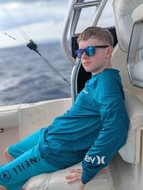 A young boy relaxes on a fishing boat, showcasing a perfect day on the ocean. His stylish sunglasses and fishing gear highlight the fun of a family fishing trip.