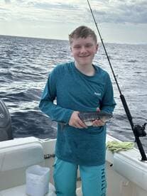 A young boy proudly holds up his catch while fishing on a boat in the open ocean, showcasing the excitement of a successful fishing trip.