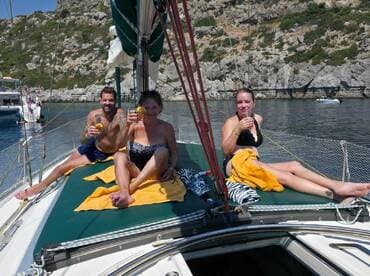 A group of friends enjoys cocktails while lounging on the deck of a sailboat, soaking up the sun and celebrating their day on the water.