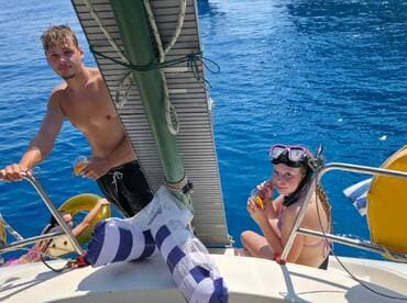 A young girl and a man enjoy refreshments on a boat, with snorkeling gear visible, capturing a fun moment on the water.
