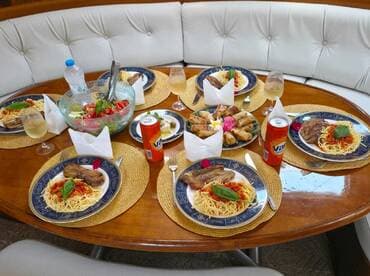 A beautifully arranged dining table on a boat featuring a delicious spread of pasta, salad, and drinks, perfect for onboard dining experiences.