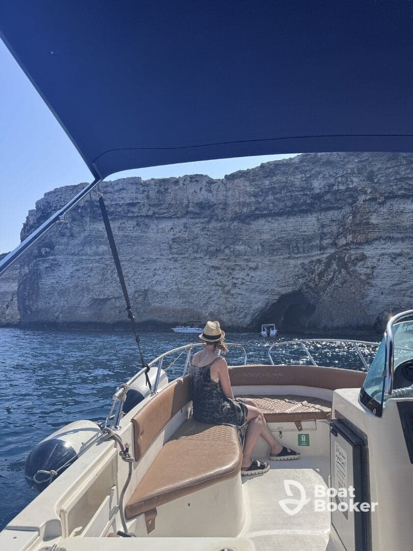 A woman relaxes on the deck of a boat, enjoying the stunning cliffside scenery — a perfect moment for unwinding on the water.
