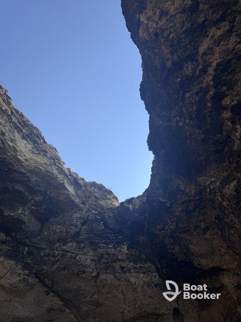 An unclear view of a rocky formation against a bright blue sky, possibly depicting a natural cave or cliff structure.