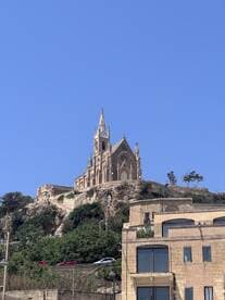 A scenic view of a church perched on a hill, surrounded by greenery and buildings, showcasing the architectural beauty of the area.