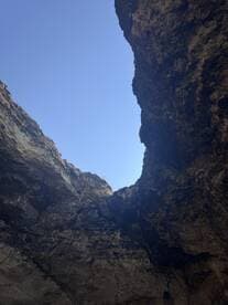 An unclear view of a rocky formation against a bright blue sky, possibly depicting a natural cave or cliff structure.