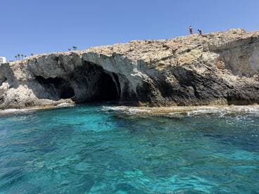 A stunning view of a rocky coastline featuring a cave, with two people enjoying the scenery above — a perfect spot for exploration and adventure.