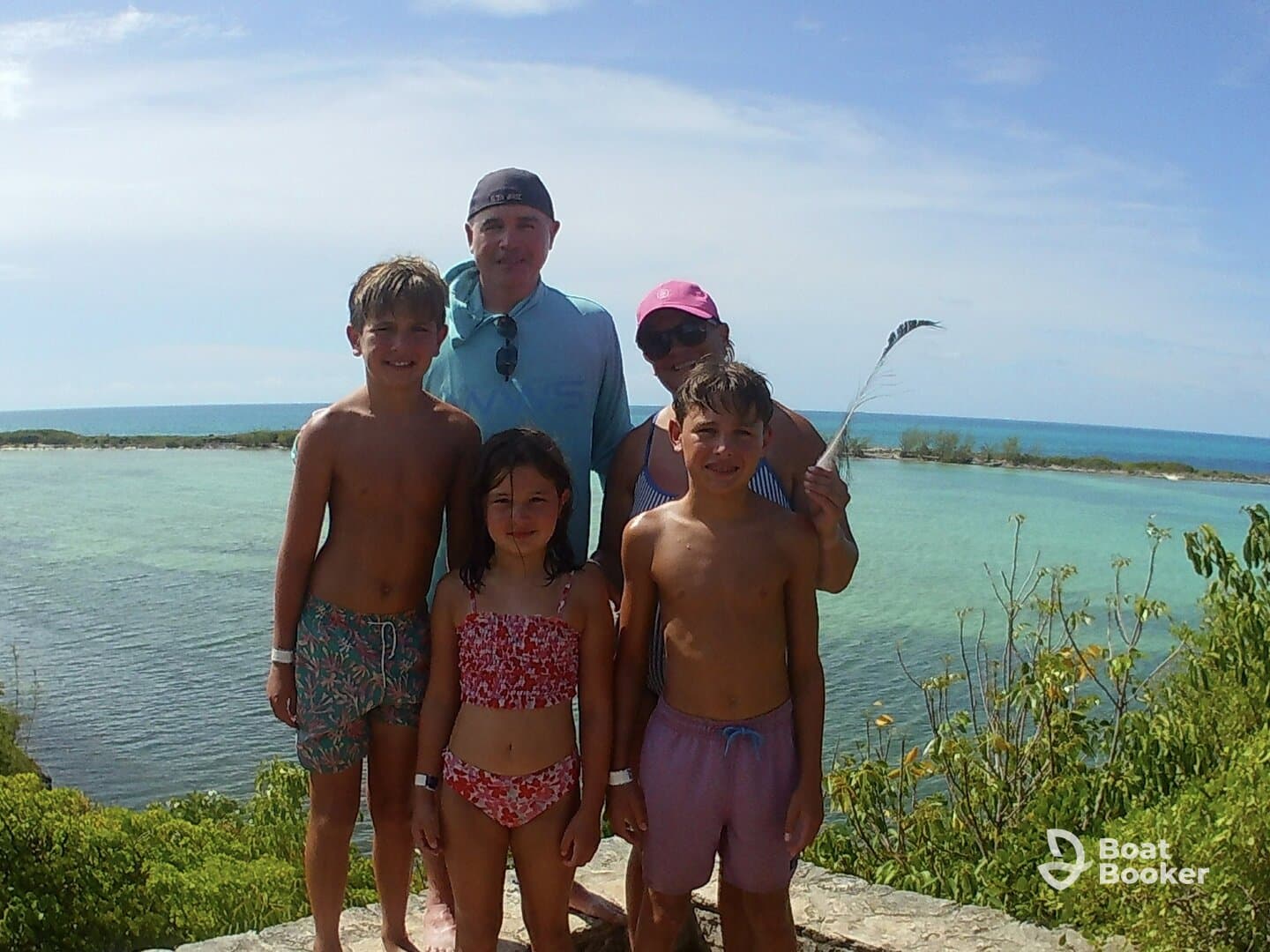 A cheerful family poses for a photo by the turquoise waters, capturing a memorable vacation moment in a beautiful beach setting.