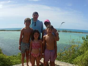A cheerful family poses for a photo by the turquoise waters, capturing a memorable vacation moment in a beautiful beach setting.