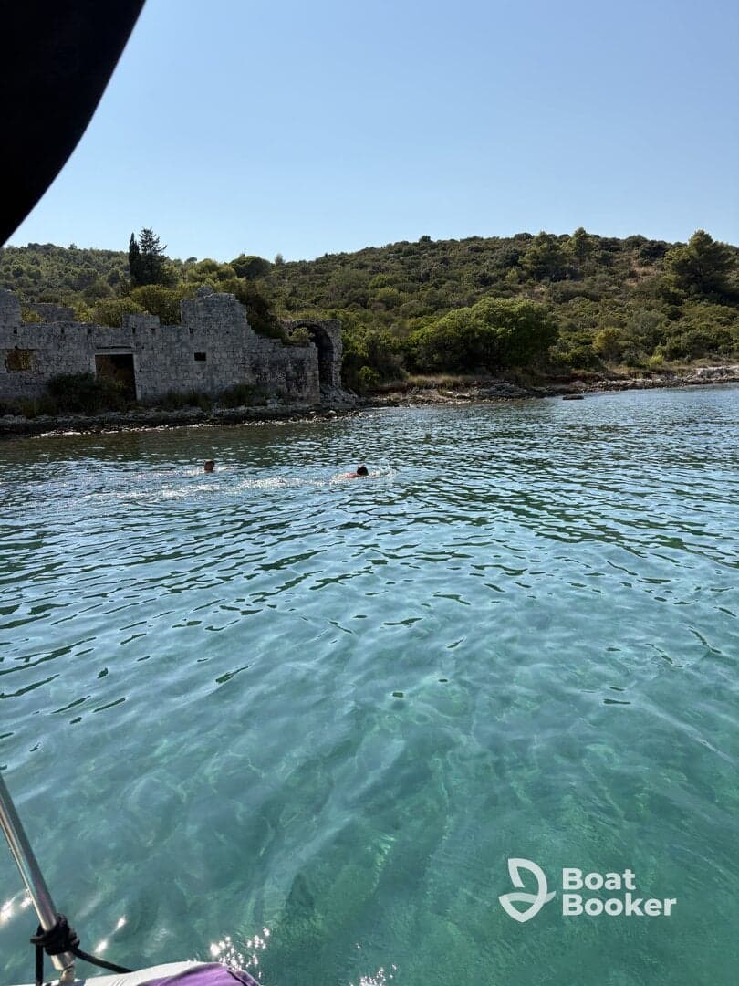 Two swimmers enjoy the crystal-clear waters near ancient ruins, creating a picturesque scene perfect for summer adventures.