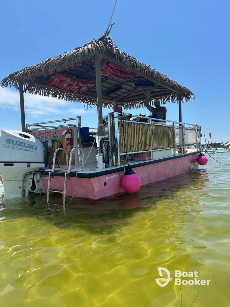 A vibrant tiki boat with a thatched roof is anchored in shallow waters, showcasing its unique design and inviting atmosphere for fun on the water.