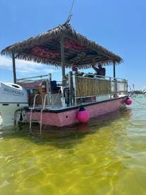 A vibrant tiki boat with a thatched roof is anchored in shallow waters, showcasing its unique design and inviting atmosphere for fun on the water.