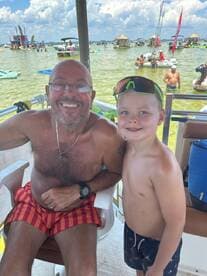 A joyful moment captured with a man and a child smiling together on a boat, surrounded by a lively water scene — perfect for family fun and summer adventures.